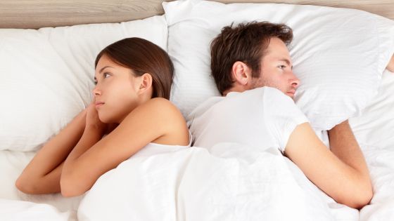 Couple lying in bed with backs to each other, staring.
