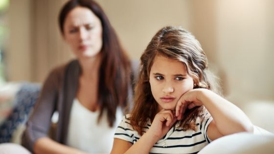 Mom sitting on couch looking at little girl with her back to her
